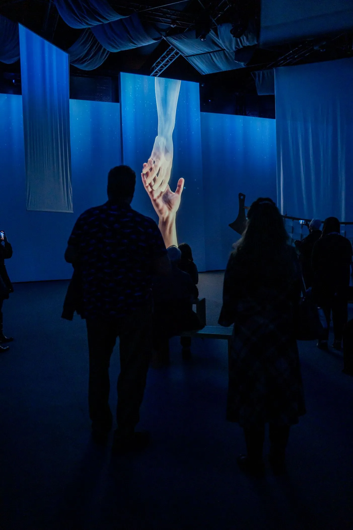 Visitors silhouetted against a blue projected scene.